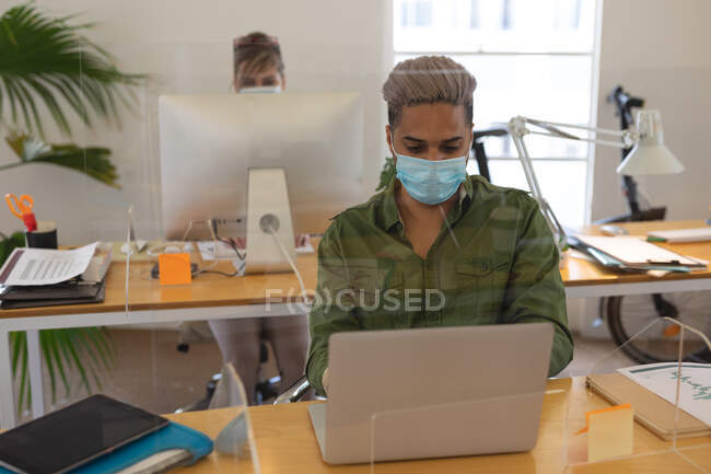 Multiethnische Gruppe männlicher und weiblicher Kreativer, die an Schreibtischen mit Schutzschirmen arbeiten und Computer benutzen. Gesundheit und Hygiene am Arbeitsplatz während der Coronavirus Covid 19 Pandemie. — Stockfoto