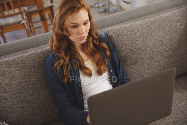 Caucasian woman spending time at home, in the living room, working from home, using her laptop, siting on a sofa. Social distancing during Covid 19 Coronavirus quarantine lockdown. — Stock Photo