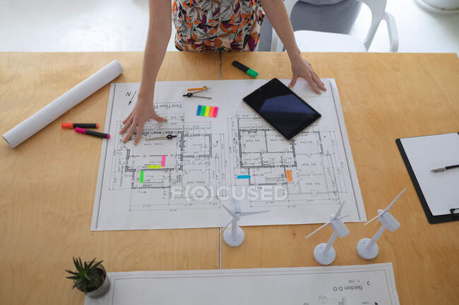 Жіночий архітектор в офісі стоїть за столом, дивлячись на архітектурний малюнок. Здоров 