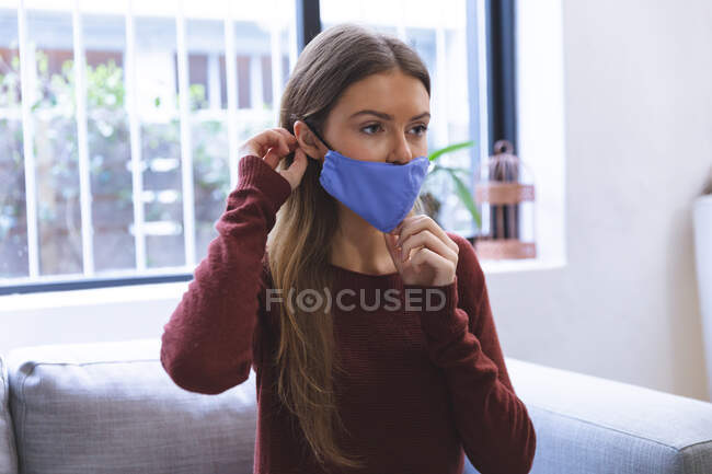 Caucasian woman spending time at home, sitting in living room, putting face mask on. Social distancing during Covid 19 Coronavirus quarantine lockdown — Stock Photo