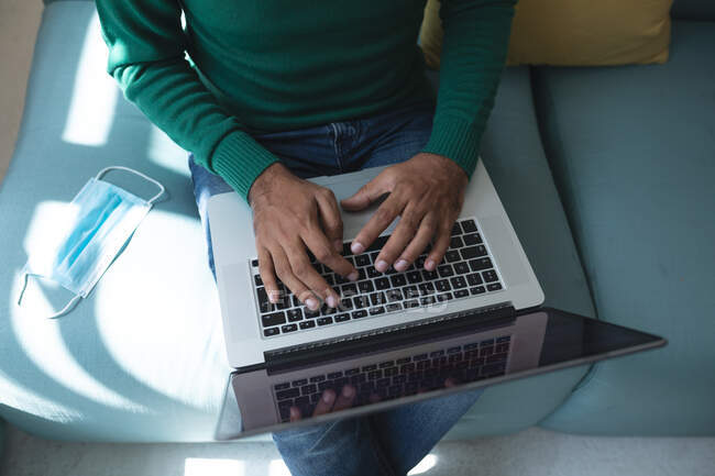 Мужчина бизнес-креатив, сидящий на диване в офисе с маской рядом с ним, используя его ноутбук. Здоровье и гиперактивность на рабочем месте во время коронавируса Ковид 19 пандемии. — стоковое фото
