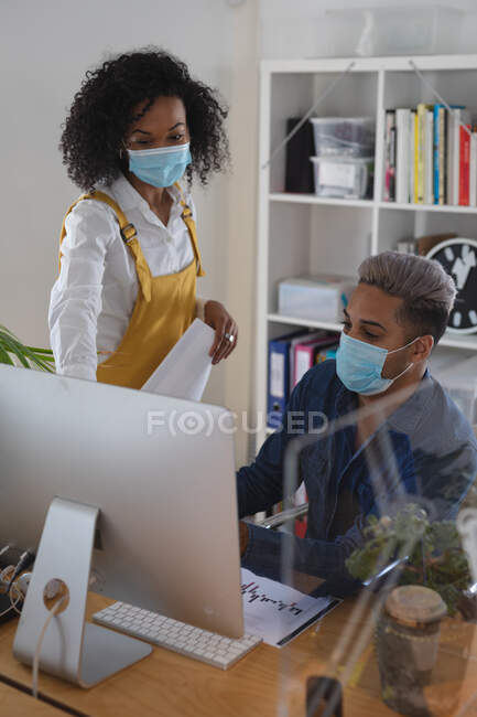 Mixte homme et femme créative collègue d'affaires parler au bureau portant des masques faciaux, à l'aide d'un ordinateur. Santé et hygiène sur le lieu de travail pendant la pandémie de Coronavirus Covid 19. — Photo de stock