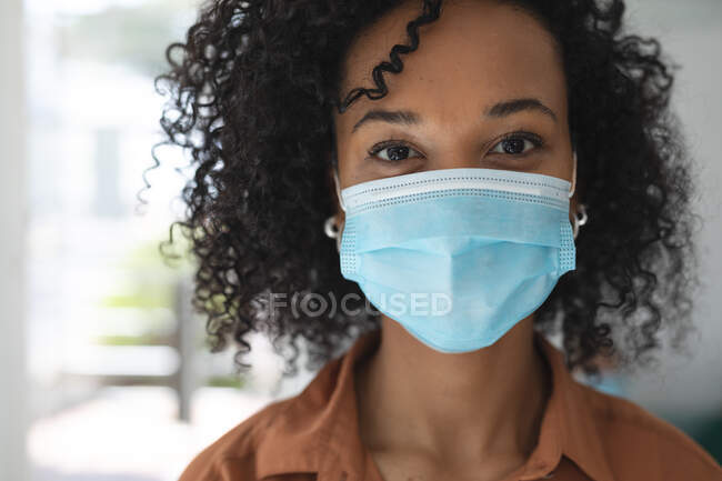 Porträt einer kreativen Geschäftsfrau mit gemischter Rasse, die in einem Büro mit Gesichtsmaske steht. Gesundheit und Hygiene am Arbeitsplatz während der Coronavirus Covid 19 Pandemie. — Stockfoto
