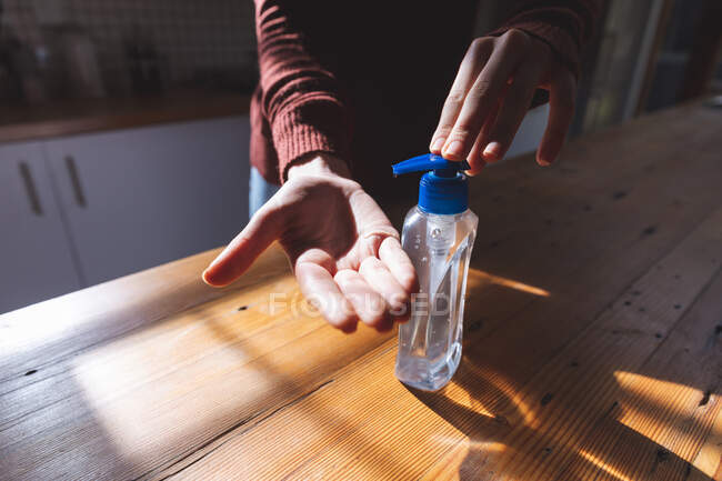 Sección media de la mujer que pasa tiempo en casa, desinfectando sus manos en la cocina. Distanciamiento social durante el bloqueo de cuarentena del Coronavirus Covid 19. - foto de stock