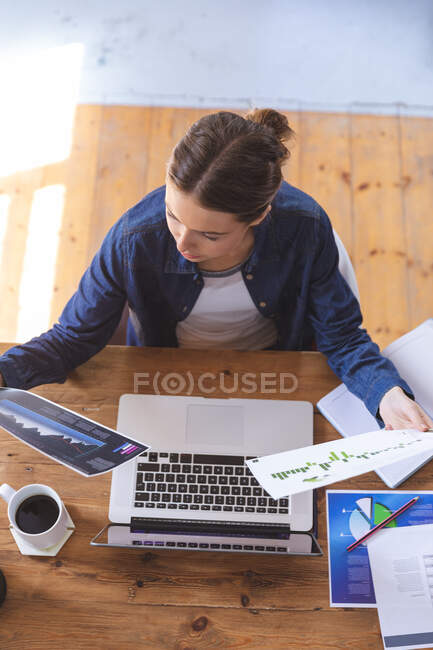 Caucasian woman spending time at home, sitting by table using laptop computer, working from home, holding paperwork. Social distancing during Covid 19 Coronavirus quarantine lockdown. — Stock Photo