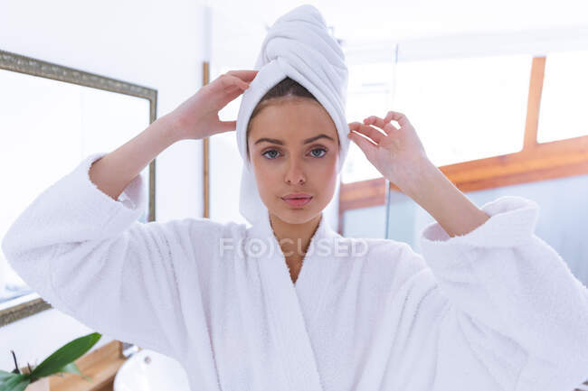 Portrait de femme caucasienne passant du temps à la maison, debout dans la salle de bain, regardant à la caméra avec une serviette autour de ses cheveux. Distance sociale pendant le confinement en quarantaine du coronavirus Covid 19. — Photo de stock