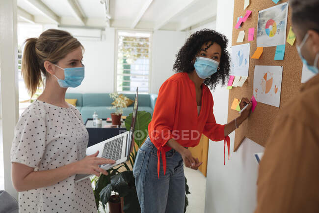 Multi ethnic group of male and female business creatives stand brainstorming in modern office wearing face masks. Health and hygiene in the workplace during Coronavirus Covid 19 pandemic. — Stock Photo