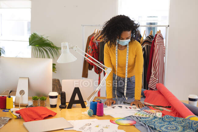 Gemischte Rasse weibliche Modedesignerin, die im Atelier mit Gesicht arbeitet. Gesundheit und Hygiene am Arbeitsplatz während der Coronavirus Covid 19 Pandemie. — Stockfoto