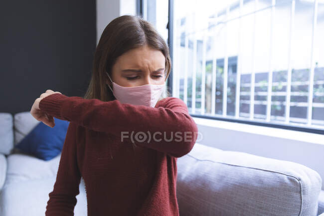 Mulher branca passando tempo em casa, sentada na sala, usando máscara facial, tosse. Distanciamento social durante o bloqueio de quarentena do Covid 19 Coronavirus. — Fotografia de Stock