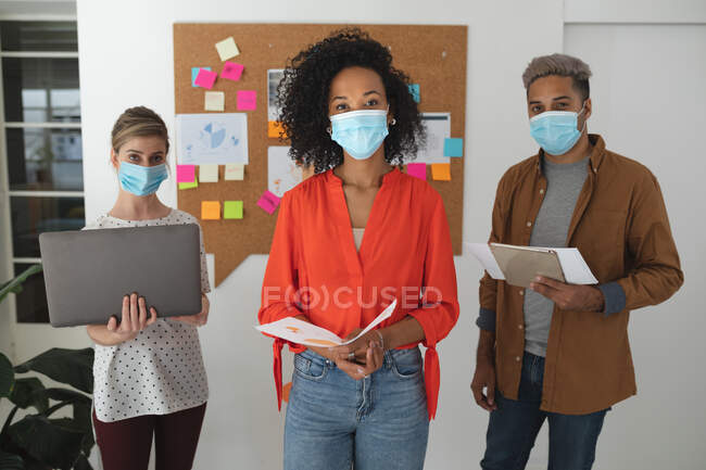 Portrait of multi ethnic group of male and female creative business colleagues wearing face masks in an office. Health and hygiene in the workplace during Coronavirus Covid 19 pandemic. — Stock Photo