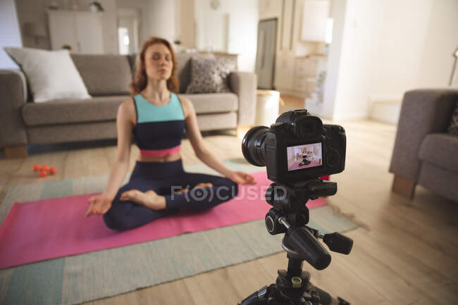 Mulher branca passando tempo em casa, na sala de estar, exercitando, praticando ioga e gravando com uma câmera. Distanciamento social durante o bloqueio de quarentena do Covid 19 Coronavirus. — Fotografia de Stock