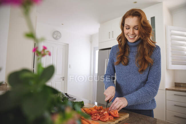 Femme blanche passant du temps à la maison, hachant des légumes dans la cuisine, souriant. Distance sociale pendant le confinement en quarantaine du coronavirus Covid 19. — Photo de stock