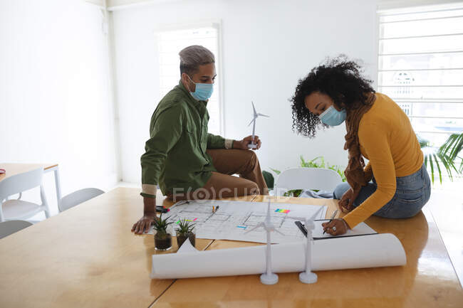 Gemischte Rassen männliche und weibliche Architekten im Büro tragen Gesichtsmasken und diskutieren über architektonische Zeichnungen. Gesundheit und Hygiene am Arbeitsplatz während der Coronavirus Covid 19 Pandemie. — Stockfoto