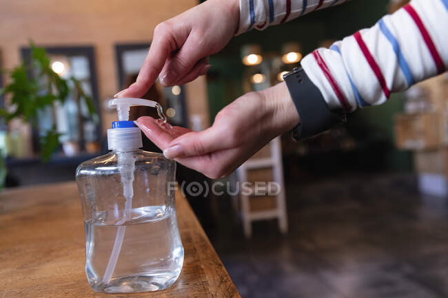 Mid section of female hairdresser working in hair salon, applying hand sanitizer on her hands. Health and hygiene in workplace during Coronavirus Covid 19 pandemic. — Stock Photo