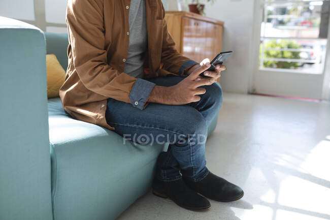 Ein kreativer Geschäftsmann sitzt mit seinem Smartphone auf dem Sofa in einem Büro. Gesundheit und Hygiene am Arbeitsplatz während der Coronavirus Covid 19 Pandemie. — Stockfoto