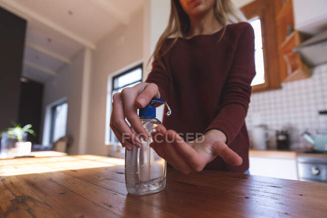 No meio da seção da mulher caucasiana passando tempo em casa, higienizando as mãos na cozinha. Distanciamento social durante o bloqueio de quarentena do Covid 19 Coronavirus. — Fotografia de Stock