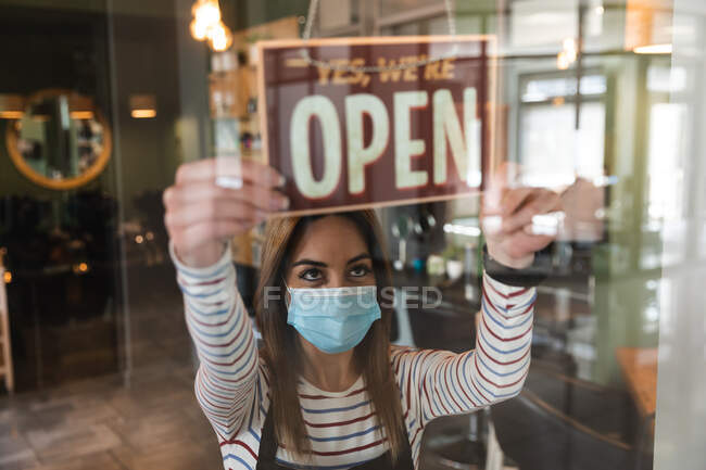 Caucasian female hairdresser working in hair salon wearing face mask, holding Yes, We Are Open sign. Health and hygiene in workplace during Coronavirus Covid 19 pandemic. — Stock Photo