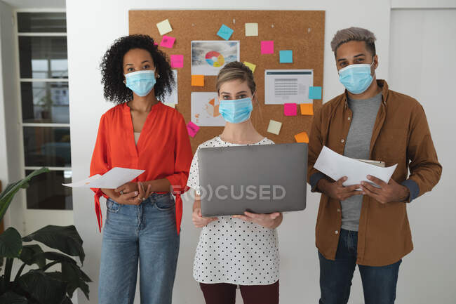 Retrato de un grupo multiétnico de colegas de negocios creativos masculinos y femeninos que usan máscaras faciales en una oficina. Salud e higiene en el lugar de trabajo durante la pandemia de Coronavirus Covid 19. - foto de stock