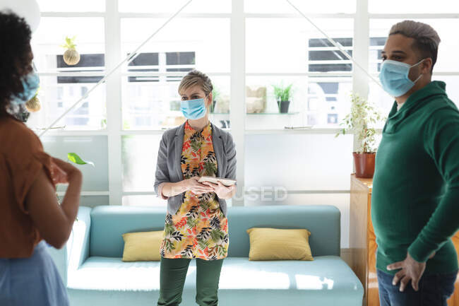 Multi ethnic group of male and female business creatives wearing face masks in office brainstorming using tablet. Health and hygiene in the workplace during Coronavirus Covid 19 pandemic. — Stock Photo