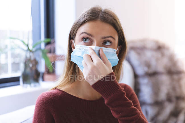 Caucasian woman spending time at home, sitting in living room, wearing face mask on. Social distancing during Covid 19 Coronavirus quarantine lockdown — Stock Photo