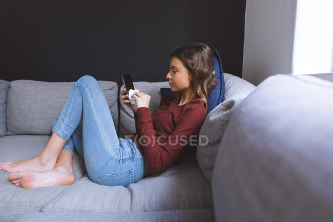 Kaukasische Frau verbringt Zeit zu Hause, sitzt im Wohnzimmer auf dem Sofa und wischt ihr Smartphone mit Taschentuch ab. Soziale Distanzierung während Covid 19 Coronavirus Quarantäne Lockdown. — Stockfoto