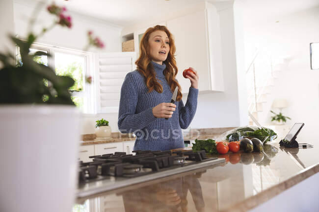 Femme caucasienne passant du temps à la maison, coupant des légumes dans la cuisine, l'enregistrant avec une caméra. Distance sociale pendant le confinement en quarantaine du coronavirus Covid 19. — Photo de stock