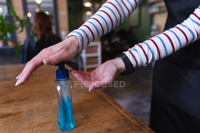 Mid section of female hairdresser working in hair salon, applying hand sanitizer on her hands. Health and hygiene in workplace during Coronavirus Covid 19 pandemic. — Stock Photo