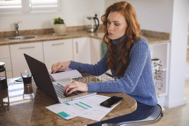 Caucasian woman spending time at home, in the kitchen, working from home, using her laptop. Social distancing during Covid 19 Coronavirus quarantine lockdown. — Stock Photo