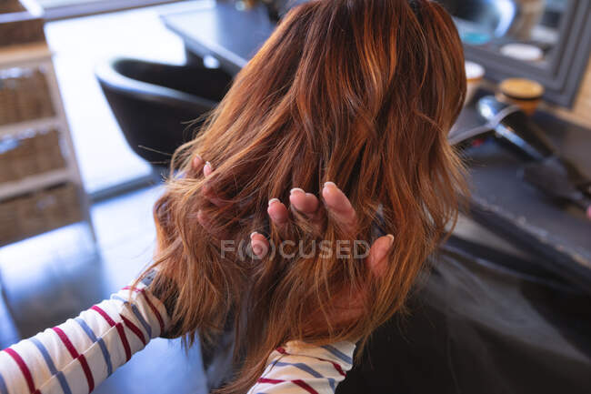 Кавказька жіноча перукарка, що працює в салоні волосся, проходить через волосся жінки-кавказького клієнта з пальцями. Здоров 