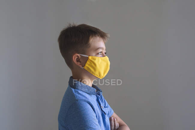 Side view of Caucasian boy spending time at home, wearing yellow face mask looking at camera on grey background. Social distancing during Covid 19 Coronavirus quarantine lockdown. — Stock Photo
