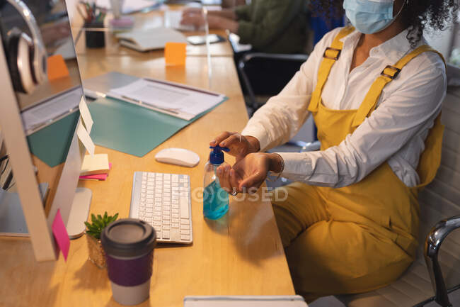 Donna creativa seduta a una scrivania in un ufficio che disinfetta le mani con disinfettante per le mani. Salute e igiene sul luogo di lavoro durante la pandemia di Coronavirus Covid 19. — Foto stock