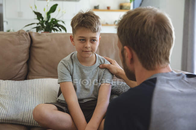 Caucasian man at home with his son together, sitting on sofa in living room, talking to each other. Social distancing during Covid 19 Coronavirus quarantine lockdown. — Stock Photo