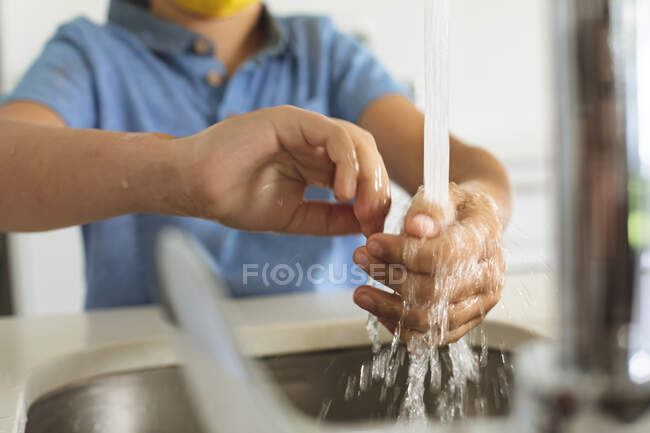 La mitad de la sección del chico pasa tiempo en casa, en la cocina lavándose las manos. Distanciamiento social durante el bloqueo de cuarentena del Coronavirus Covid 19. - foto de stock