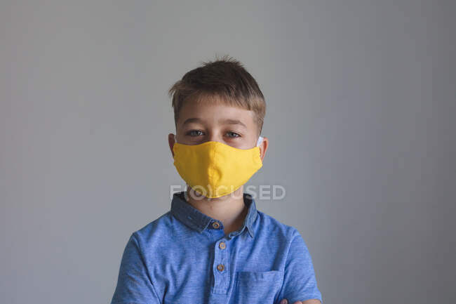 Retrato de menino caucasiano passando tempo em casa, usando máscara amarela olhando para a câmera em fundo cinza. Distanciamento social durante o bloqueio de quarentena do Covid 19 Coronavirus. — Fotografia de Stock