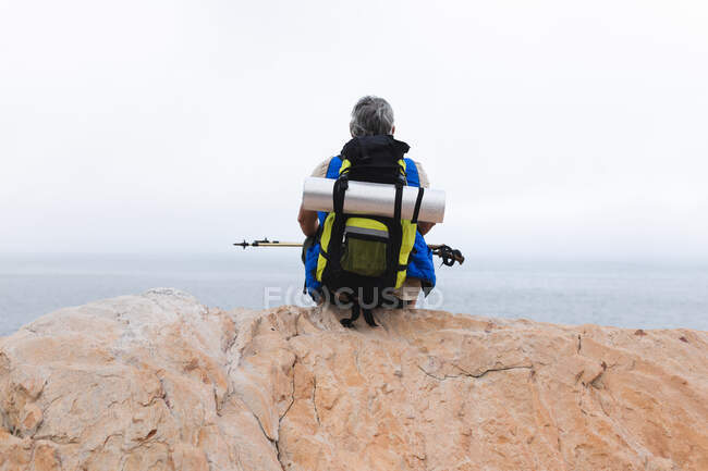 Старший чоловік проводить час у природі, гуляючи в горах, сидячи на скелі і насолоджуючись видом. здоровий спосіб життя пенсійна діяльність . — стокове фото