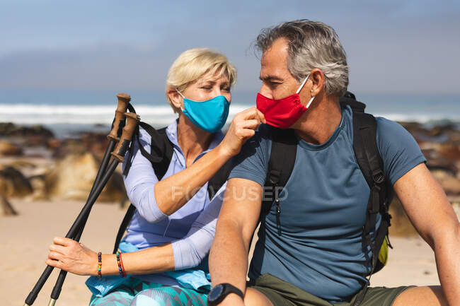 Casal sênior passando tempo na natureza juntos, andando na praia, colocando suas máscaras faciais. atividade de aposentadoria saudável. — Fotografia de Stock