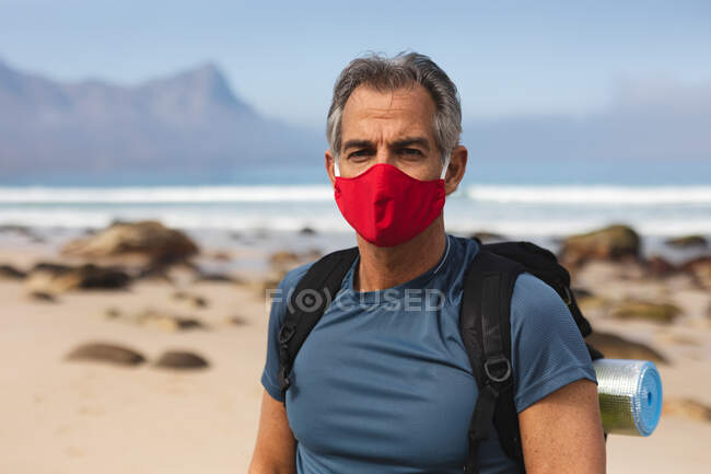 Portrait of a senior man spending time in nature, walking on the beach, wearing a face mask, looking at the camera. healthy lifestyle retirement activity. — Stock Photo