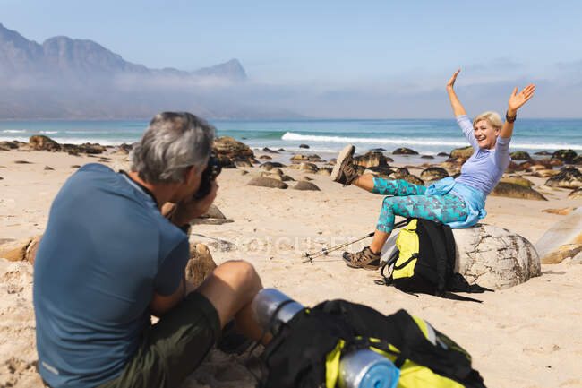 Старшая пара проводит время на природе вместе, гуляя по пляжу, мужчина фотографирует женщину. активный уход на пенсию. — стоковое фото
