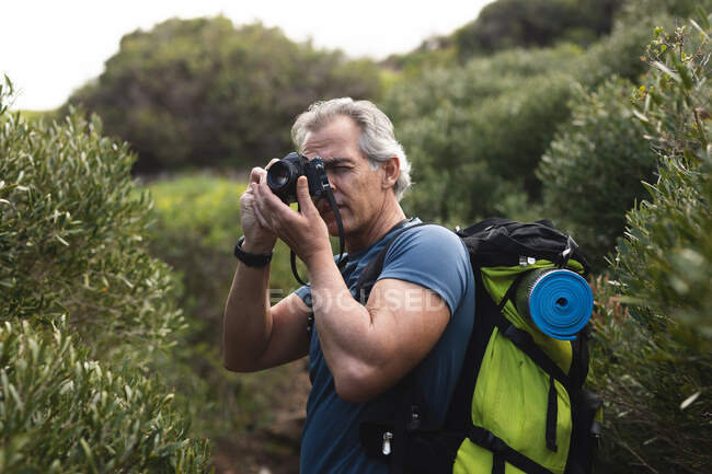 Hombre mayor pasando tiempo en la naturaleza, caminando por las montañas, tomando una foto. estilo de vida saludable actividad de jubilación. - foto de stock