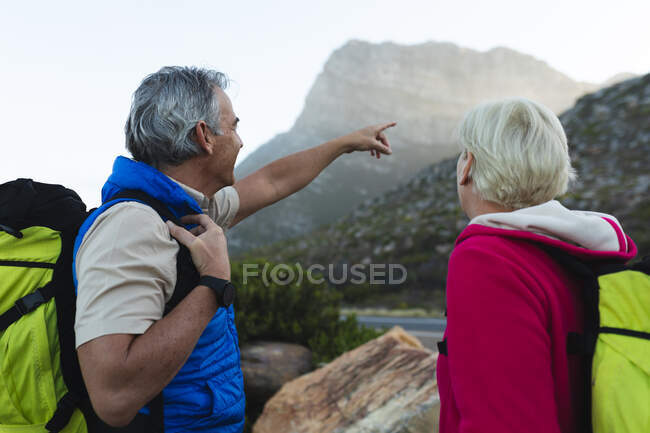 Casal sênior passando tempo na natureza juntos, andando nas montanhas, o homem está apontando para as montanhas. atividade de aposentadoria saudável. — Fotografia de Stock