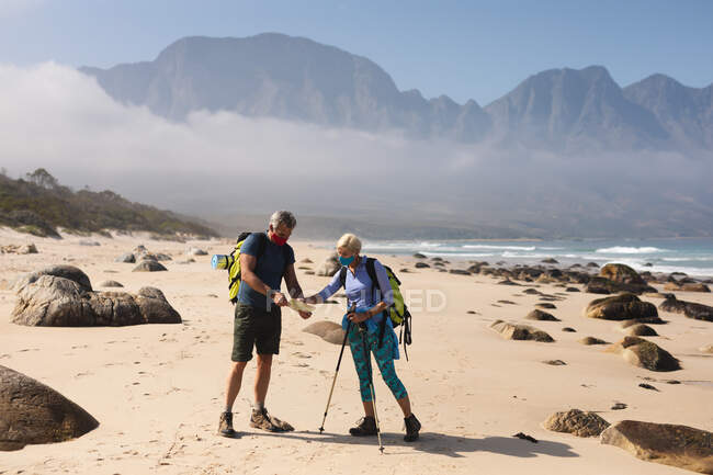 Старшая пара проводит время на природе вместе, гуляя по пляжу, надевая маски для лица, смотря на карту. активный уход на пенсию. — стоковое фото