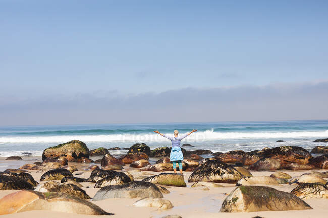 Mujer mayor pasando tiempo en la naturaleza, caminando por la playa, disfrutando de la vista, levantando los brazos. estilo de vida saludable actividad de jubilación. - foto de stock