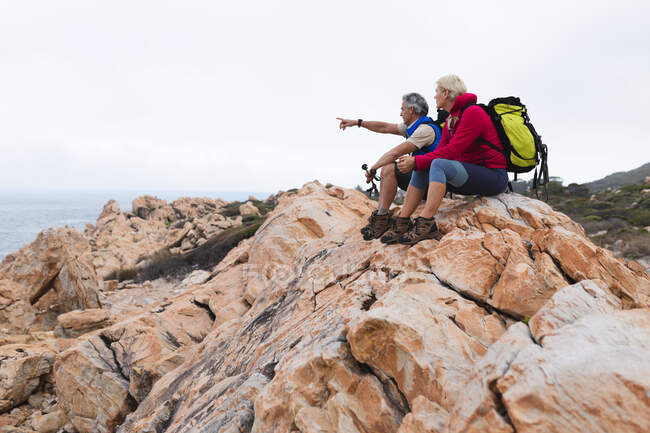 Senioren verbringen Zeit miteinander in der Natur, wandern in den Bergen, der Mann zeigt weg. Gesunder Lebensstil im Ruhestand. — Stockfoto