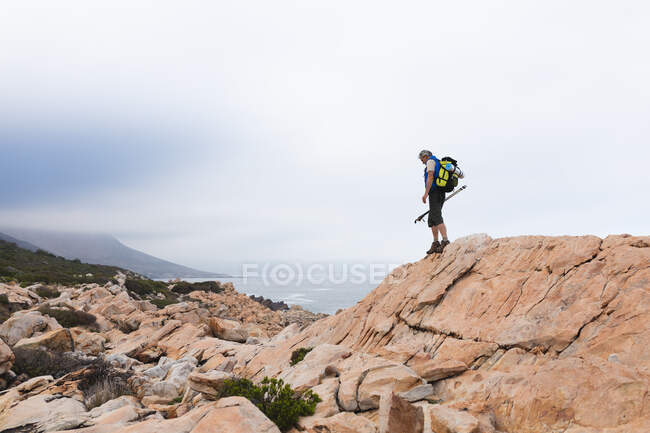 Hombre mayor pasando tiempo en la naturaleza, caminando por las montañas, caminando por un acantilado. estilo de vida saludable actividad de jubilación. - foto de stock