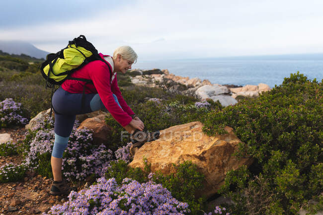 Senior woman spending time in nature, walking in the mountains, tying her shoe. healthy lifestyle retirement activity. — Stock Photo