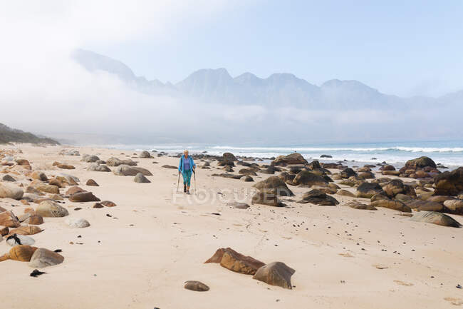 Старшая женщина проводит время на природе, гуляя по пляжу у моря. активный уход на пенсию. — стоковое фото