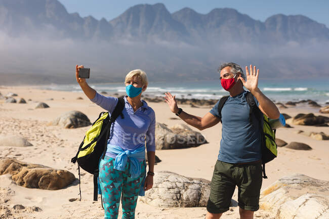 Senioren verbringen Zeit miteinander in der Natur, gehen am Strand spazieren, tragen Gesichtsmasken und machen ein Selfie. Gesunder Lebensstil im Ruhestand. — Stockfoto