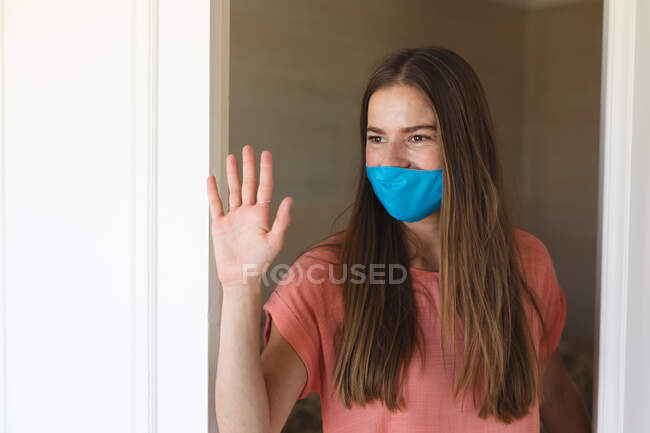 Caucasian woman waving her hand and wearing face mask.self isolation at home during coronavirus covid 19 quarantine lockdown. — Stock Photo