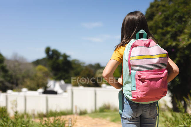 Menina caucasiana com comprimento do ombro cabelo escuro andando para a escola carregando saco escolar. educação e estilo de vida durante a pandemia do coronavírus covid 19 — Fotografia de Stock