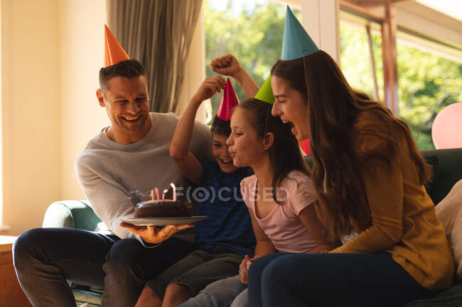 Caucasian family spending time at home together celebrating a birthday, wearing party hats and blowing candles. quality time together in coronavirus covid 19 quarantine lockdown. — Stock Photo